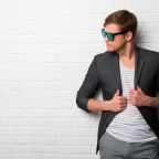 Portrait Of Smiling  stylish  man in sunglasses  Standing Against Brick Wall In Modern Office. Studio image wuth flash.