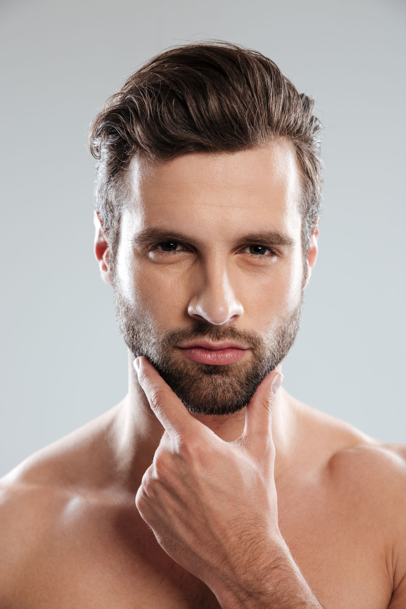 Close up portrait of a young sexy naked man touching his chin and looking at camera isolated over white background